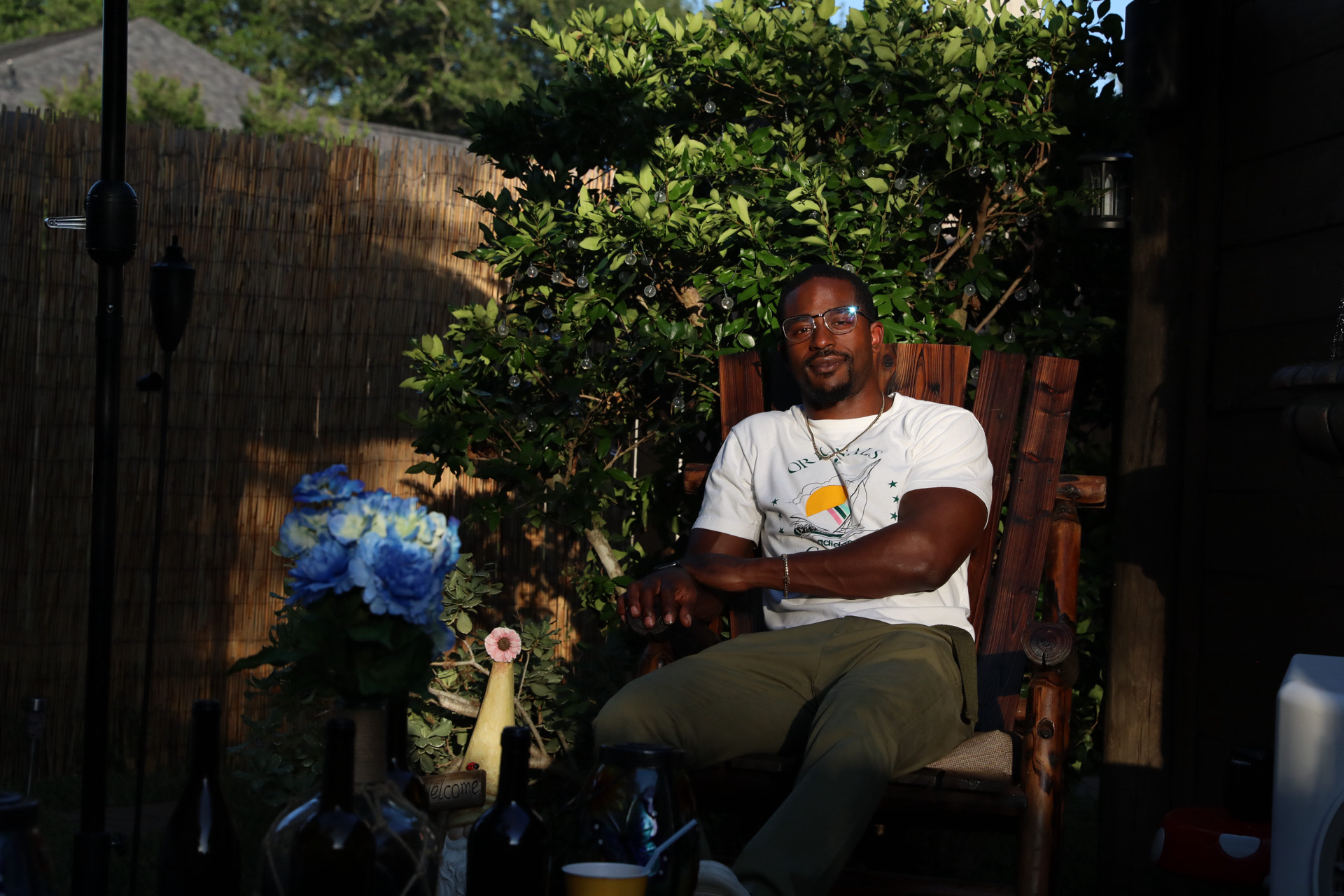 Justinn seated outdoors in a relaxed portrait surrounded by evening light and greenery.