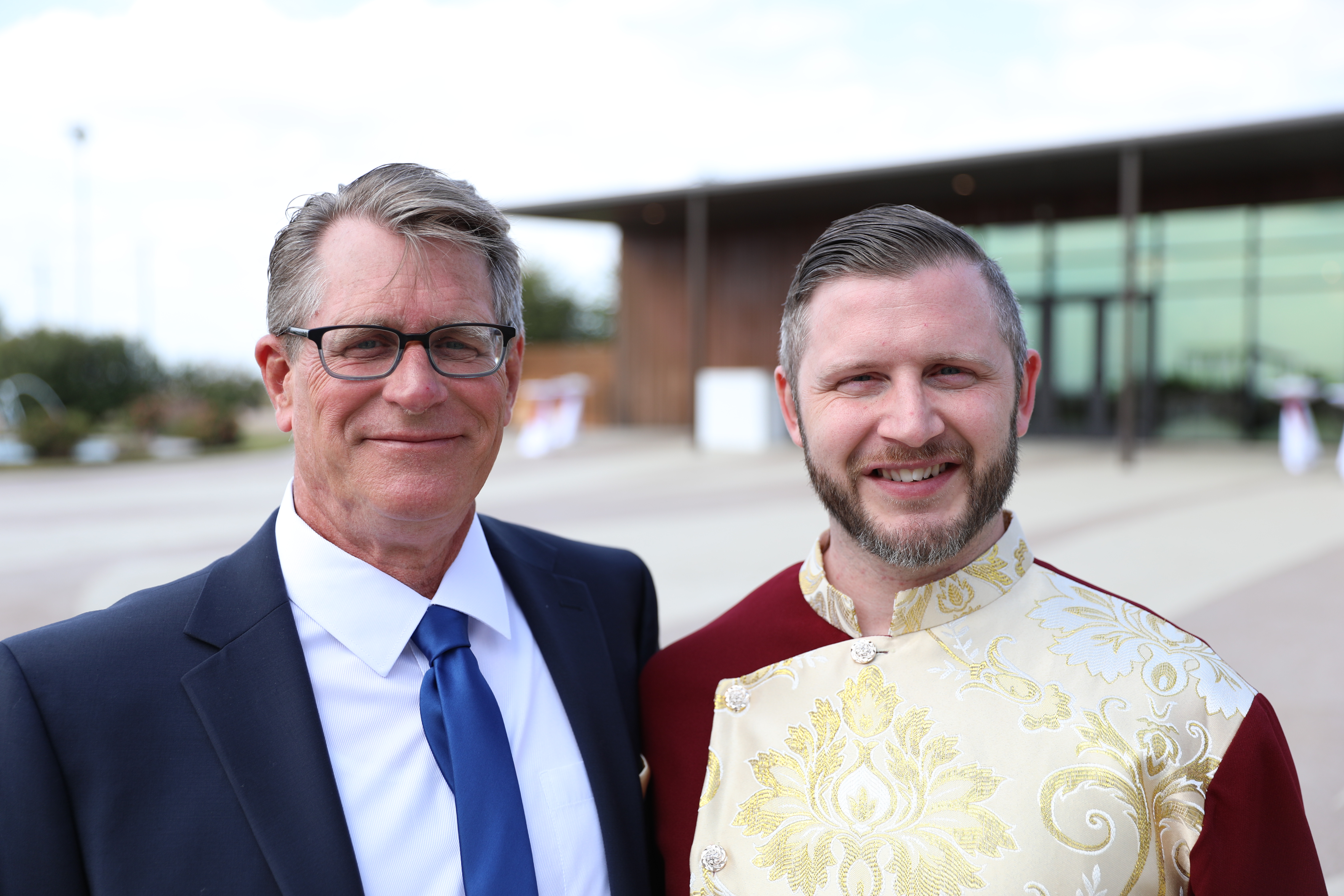 Portrait of two men smiling outdoors during a formal celebration.